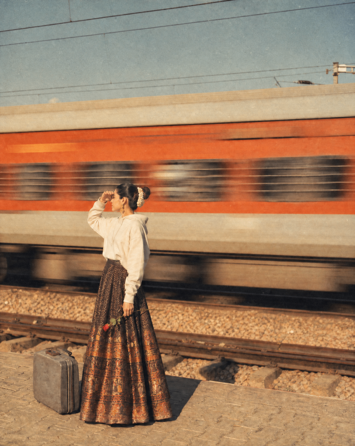 A woman in a lehenga waits on a Sydney-bound platform as a train rushes past — a quiet moment between two homes.