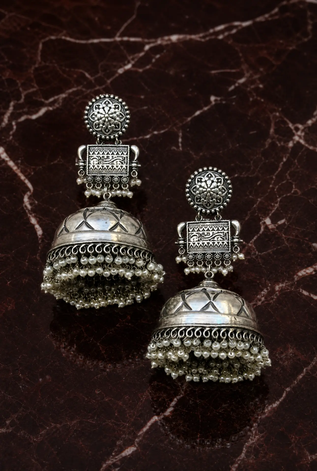 Pair of oxidised silver pearl jhumkas on dark maroon marble