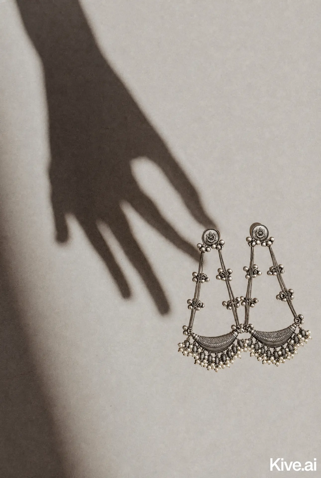 Oxidised silver chandbali earrings on an ivory surface beside a soft hand shadow